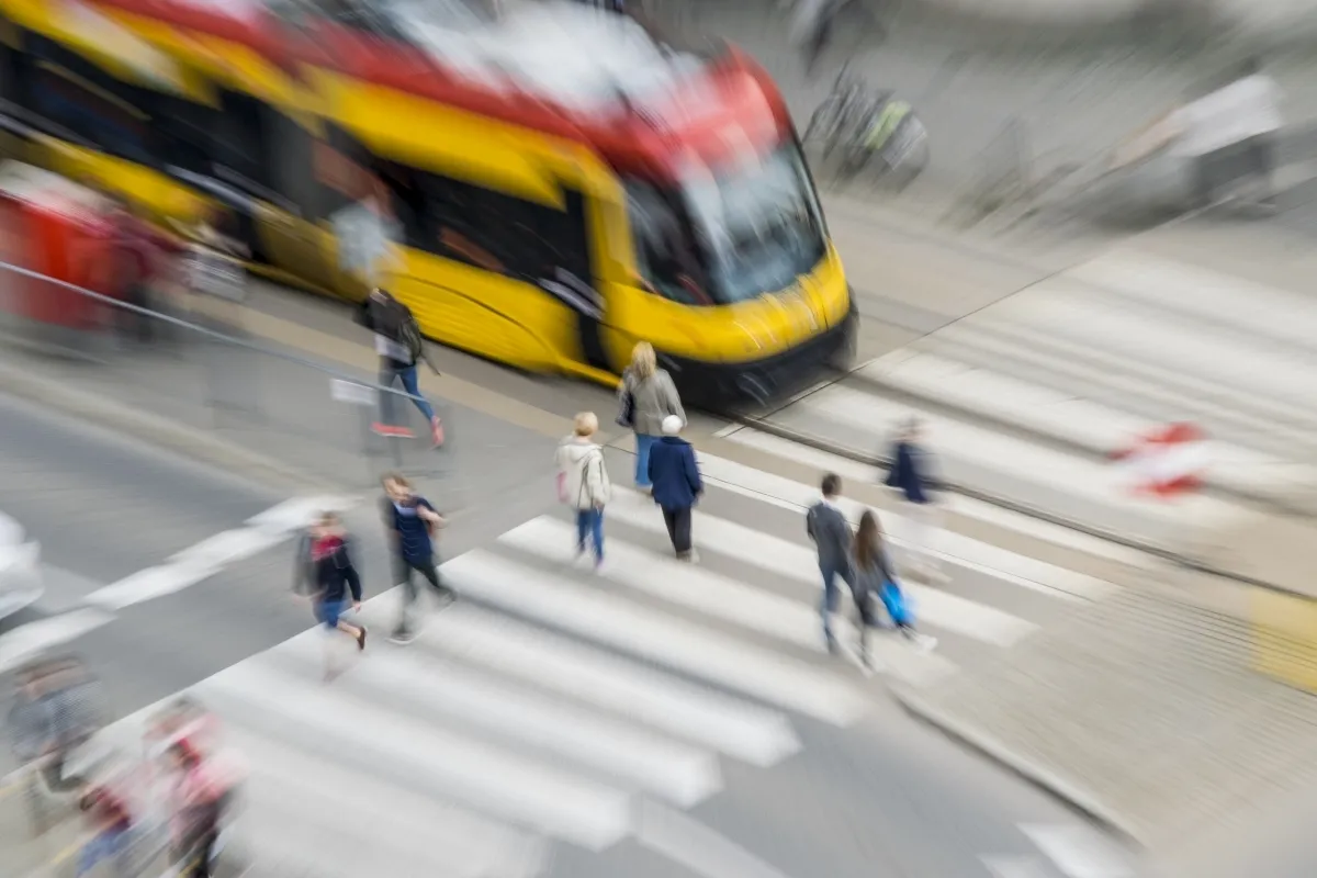Yellow tram rushing past a zebra crossing with pedestrians